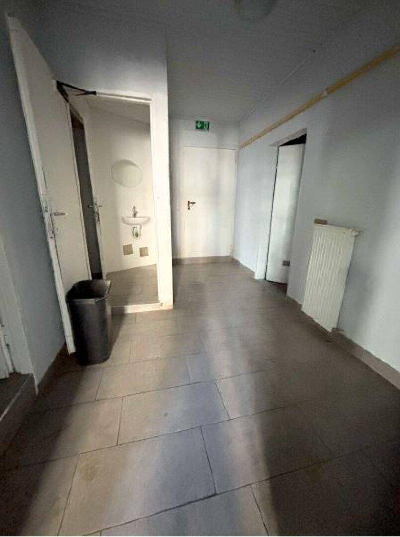 Flur mit Fliesenboden und Zugang zu einem kleinen Badezimmer mit Waschbecken und Spiegel.