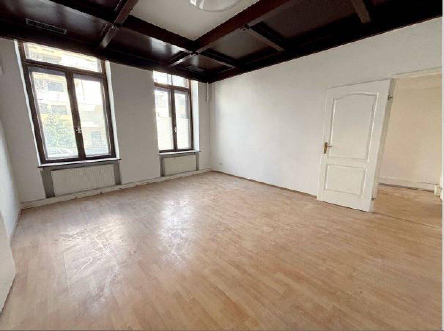Leeres Zimmer mit Holzbalkendecke, Parkettboden und großen Fenstern, bietet viel natürliches Licht.