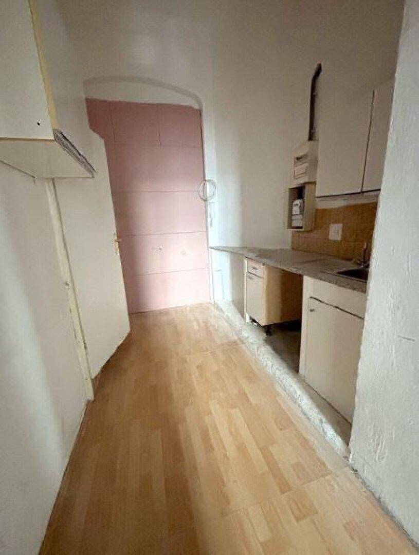 Schmale Küchenzeile mit einfachen Schränken, Spüle und Holzboden, ideal für kleine Wohnungen.