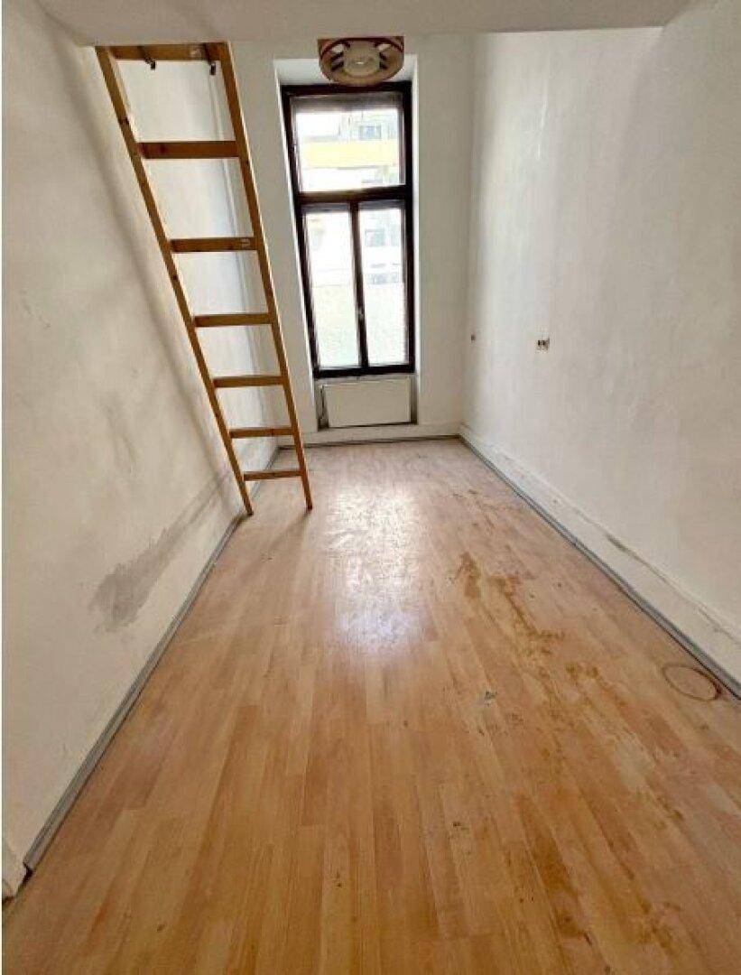 Kleines Zimmer mit Holzleiter, Holzboden und einem Fenster, das Tageslicht hereinlässt.