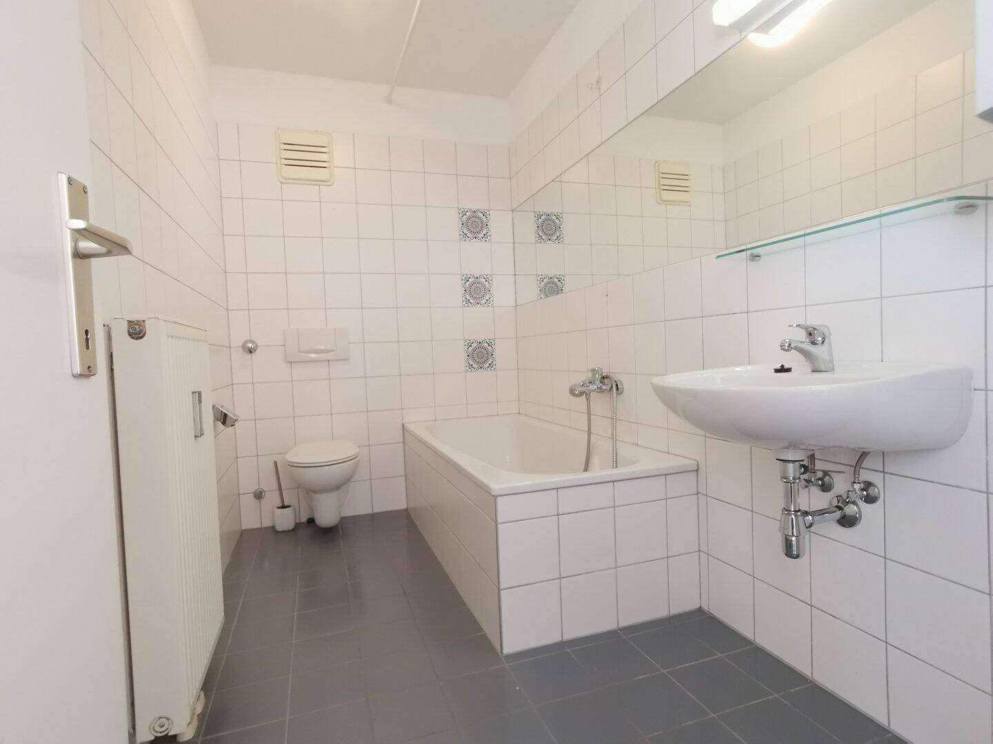 Badezimmer mit weißen Fliesen, Badewanne, Toilette und Waschbecken.