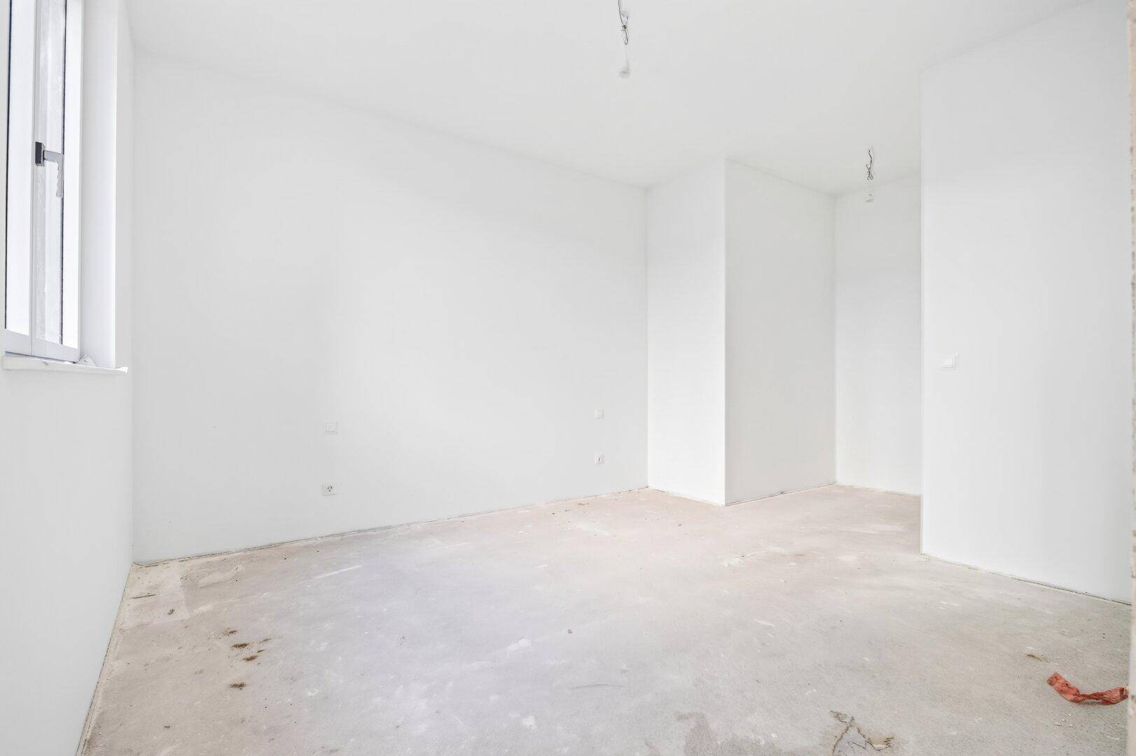 Unfertiger Raum mit weiß gestrichenen Wänden und einem Fenster, ideal für individuelle Gestaltung.