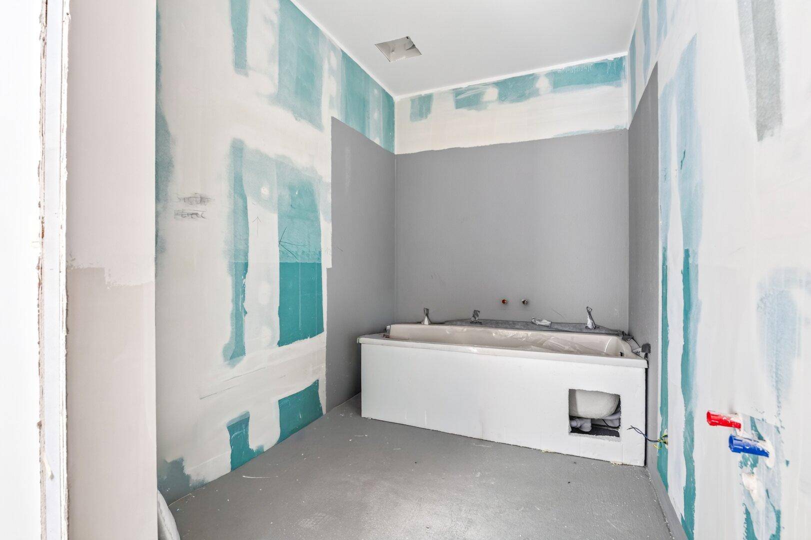 Badezimmer im Rohbau mit einer bereits installierten Badewanne und vorbereiteten Wänden.