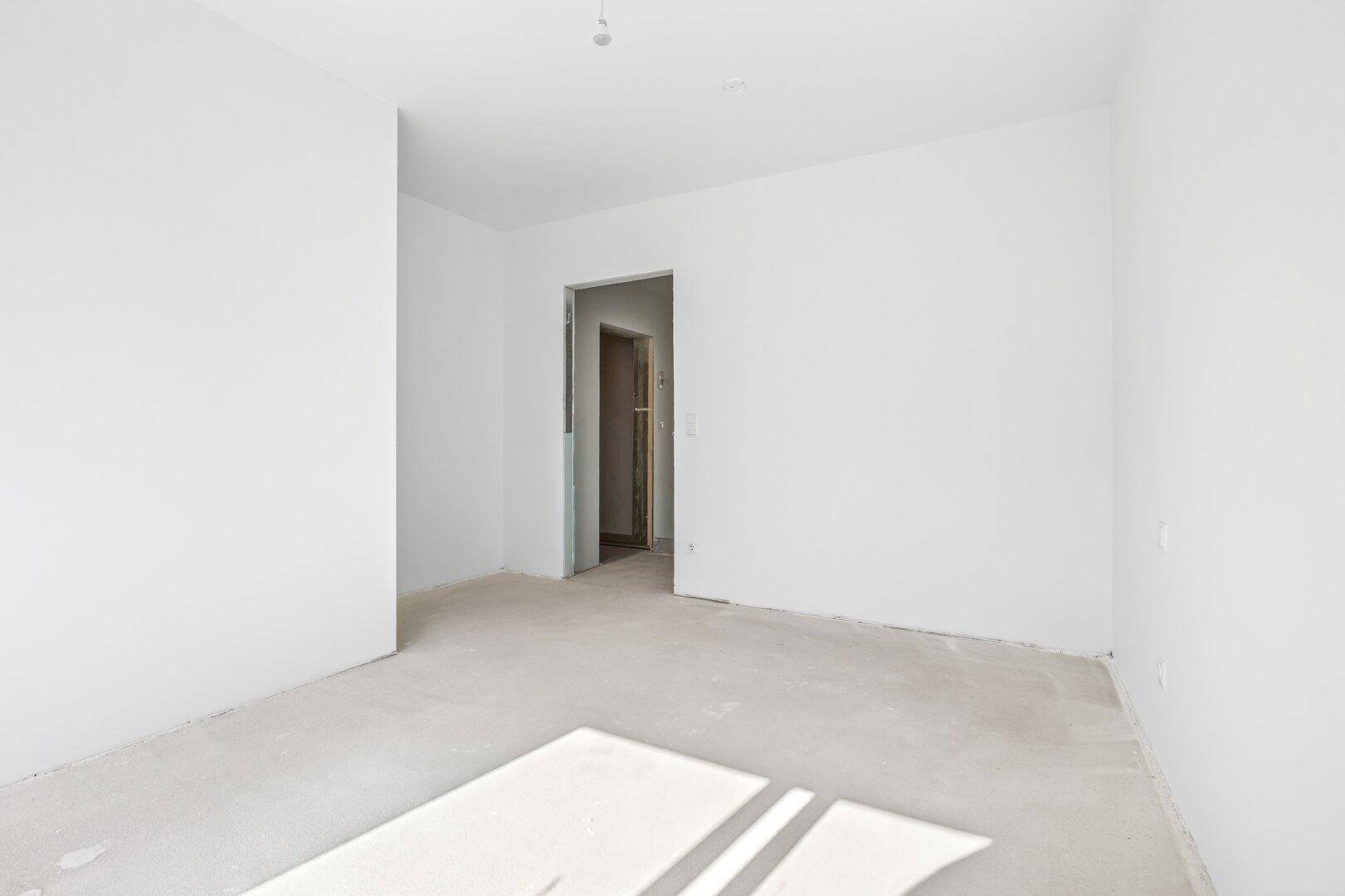Leerer Raum mit weiß gestrichenen Wänden und einem Durchgang zu einem weiteren Zimmer, mit Sonnenlicht auf dem Boden.