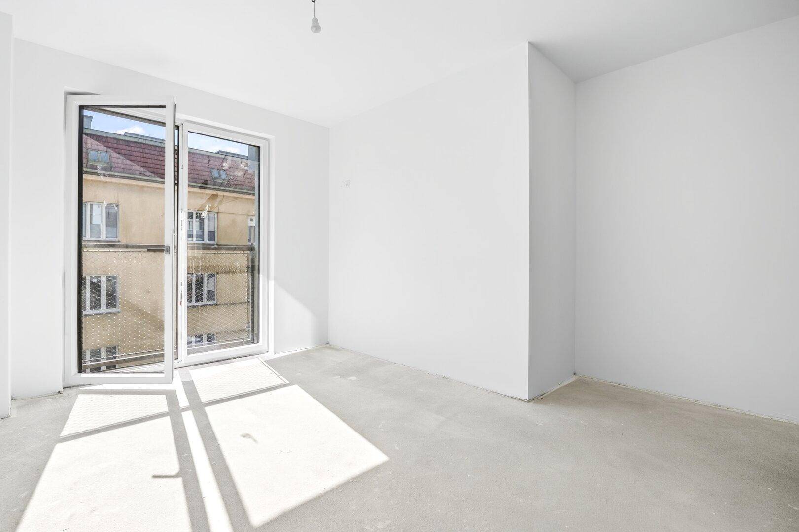 Lichtdurchfluteter Raum mit geöffnetem Fenster und französischem Balkon, der viel Tageslicht hereinlässt.