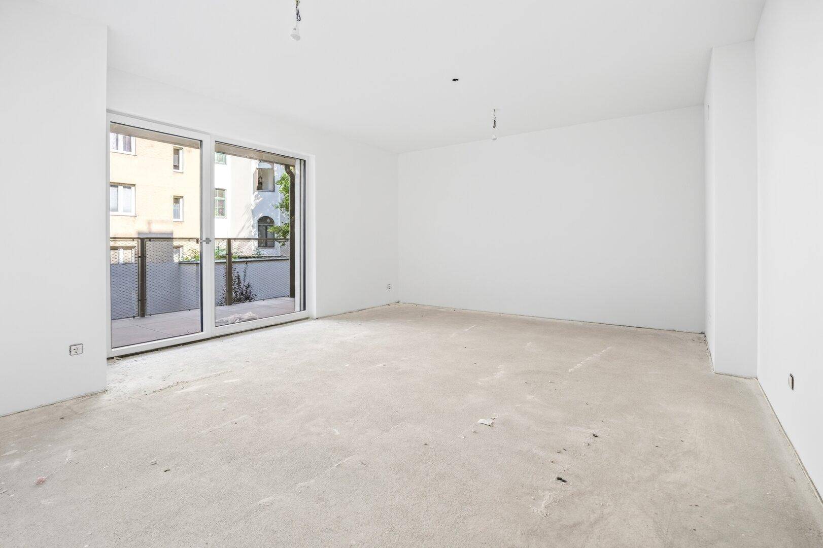 Heller, unmöblierter Raum mit großen Schiebetüren zum Balkon und Rohbetonboden, bereit für den Ausbau.