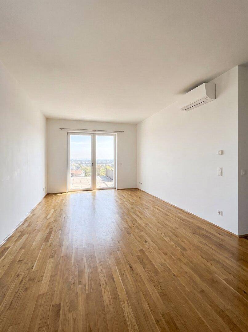 Geräumiges, helles Wohnzimmer mit Holzparkett, Klimaanlage und Zugang zu einem Außenbereich.