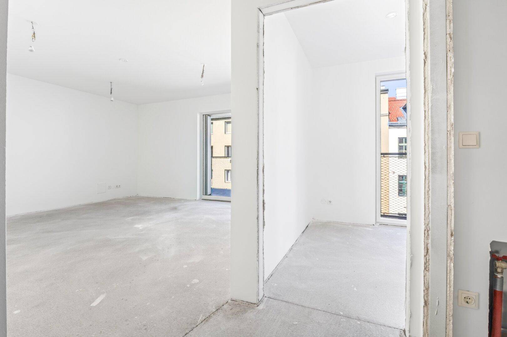 Unmöblierter Raum mit weißen Wänden und Betonboden, hell durch mehrere Fenster.