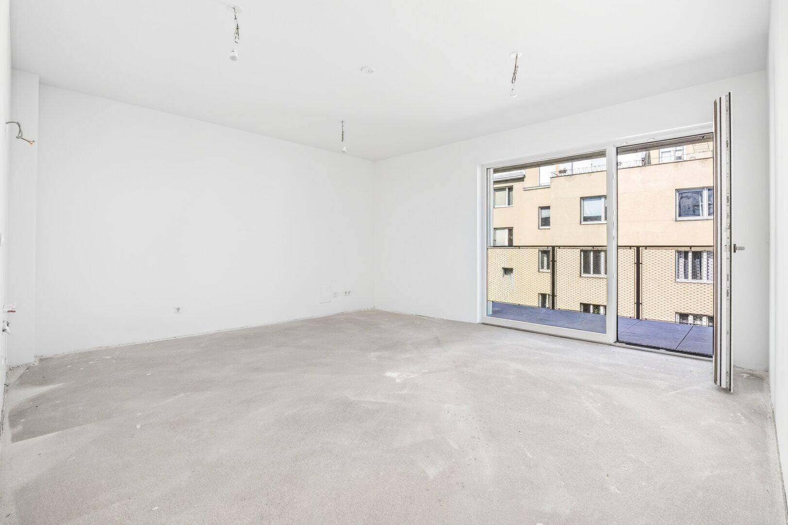 Leerer Raum mit weißen Wänden und Betonboden, ausgestattet mit einer großen Schiebetür zum Balkon.