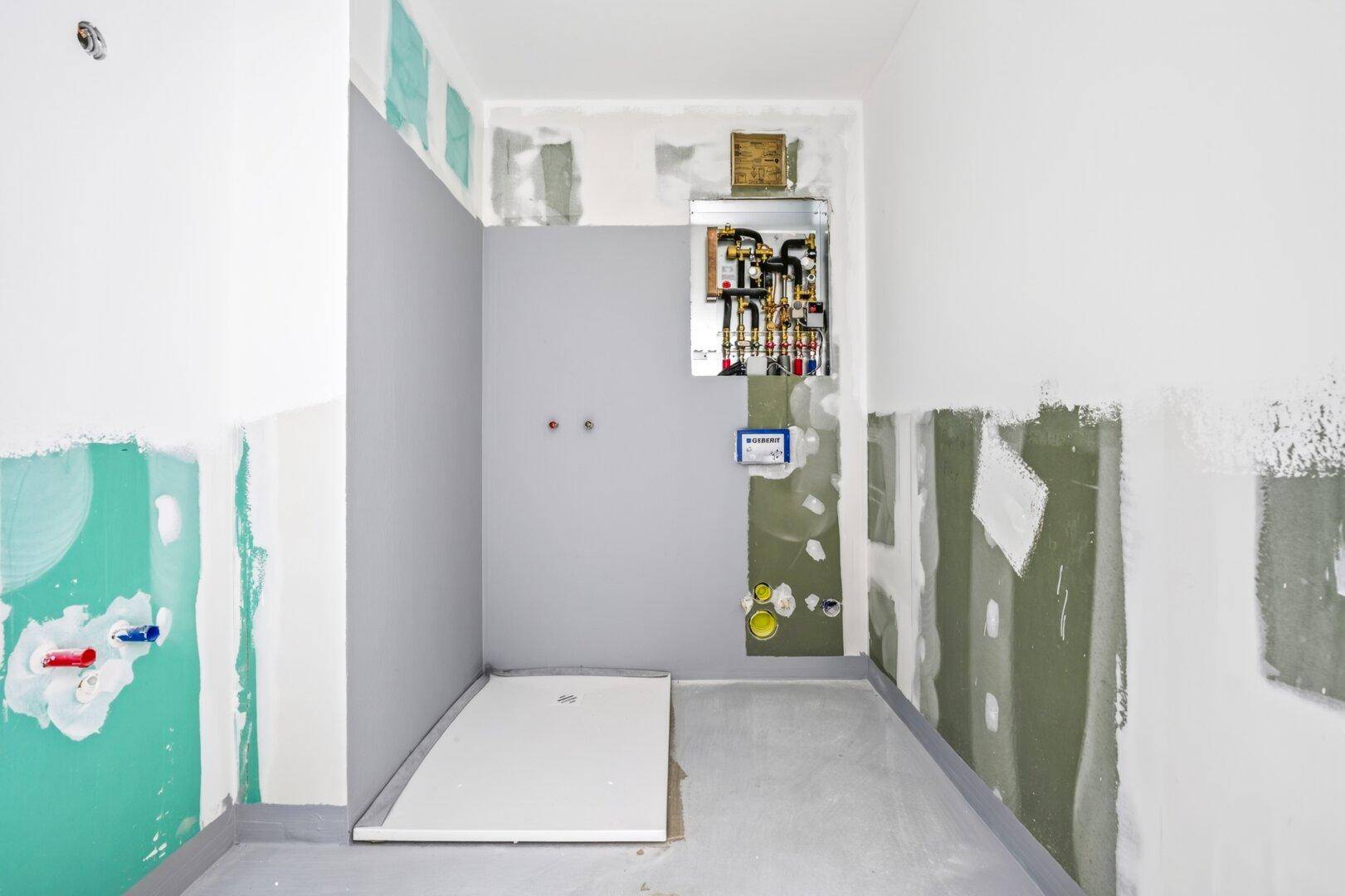 Unfertiges Badezimmer mit vorbereiteter Duschwanne und sichtbaren Sanitärinstallationen für den weiteren Ausbau.