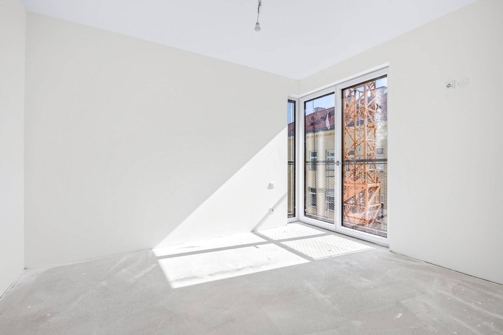 Unfertiger Wohnraum mit viel Tageslicht durch große Fenster und Blick auf die Umgebung.