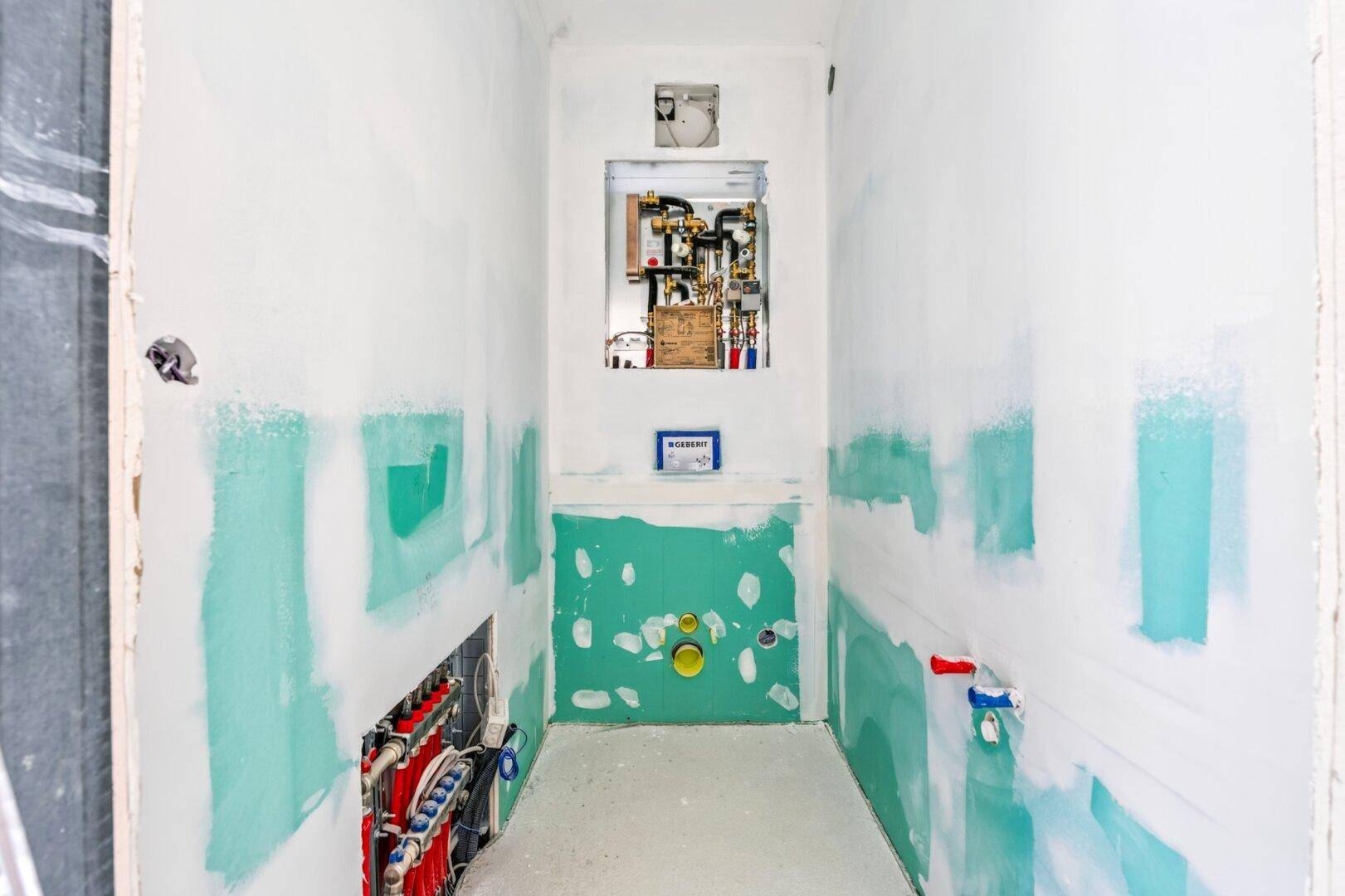 Badezimmer im Rohbau mit sichtbaren Rohrleitungen und vorbereiteten Wänden für die Fliesenverlegung.