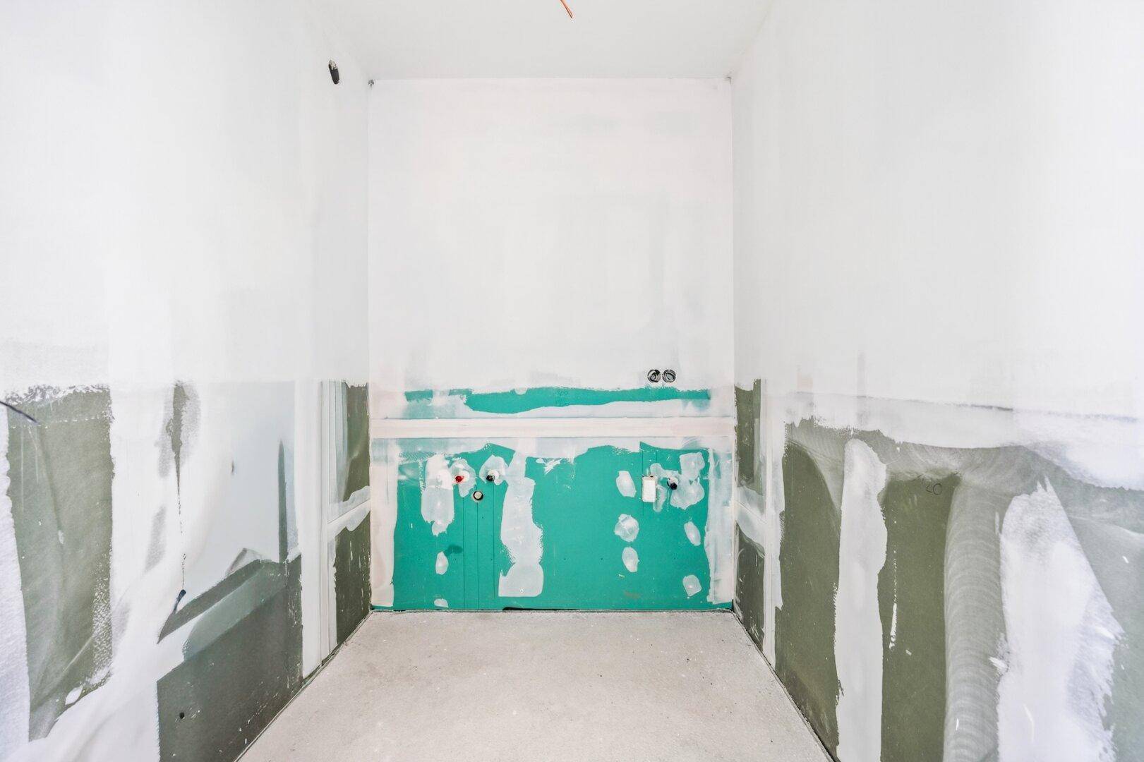 Unfertiges Badezimmer mit vorbereiteten Anschlüssen und grünen Feuchtraumplatten an den Wänden.