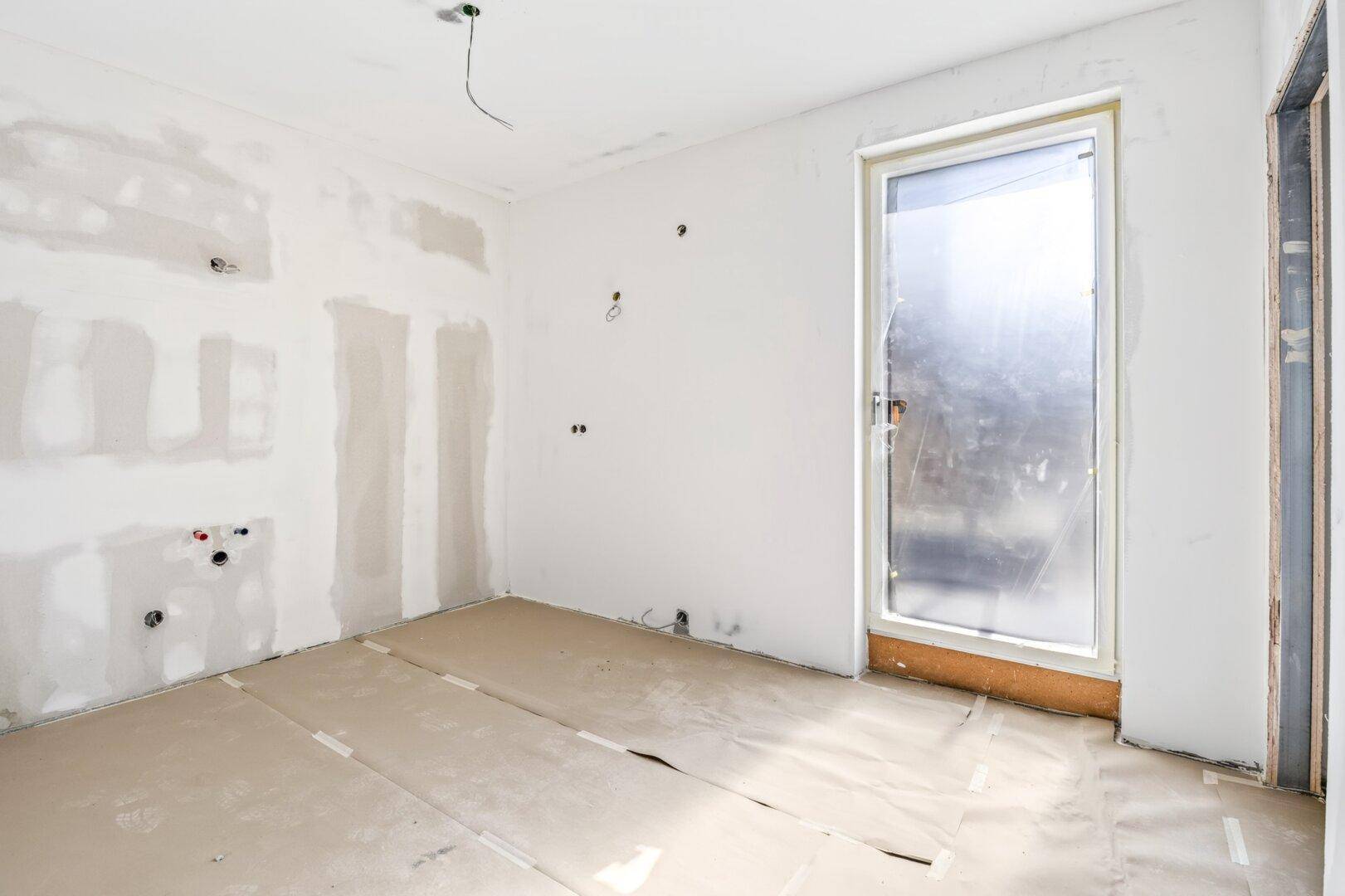 Unfertiger Raum mit Zugang zu einem Außenbereich und vorbereiteten Installationen an den Wänden.