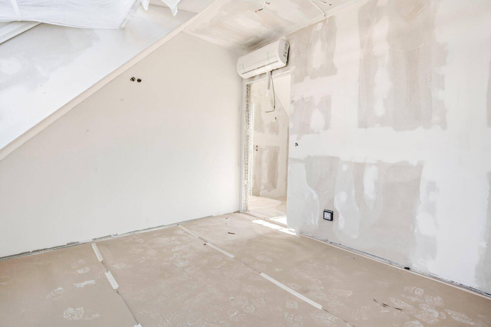 Rohbau eines Raumes mit schräger Decke und installierter Klimaanlage, bereit für den Ausbau.