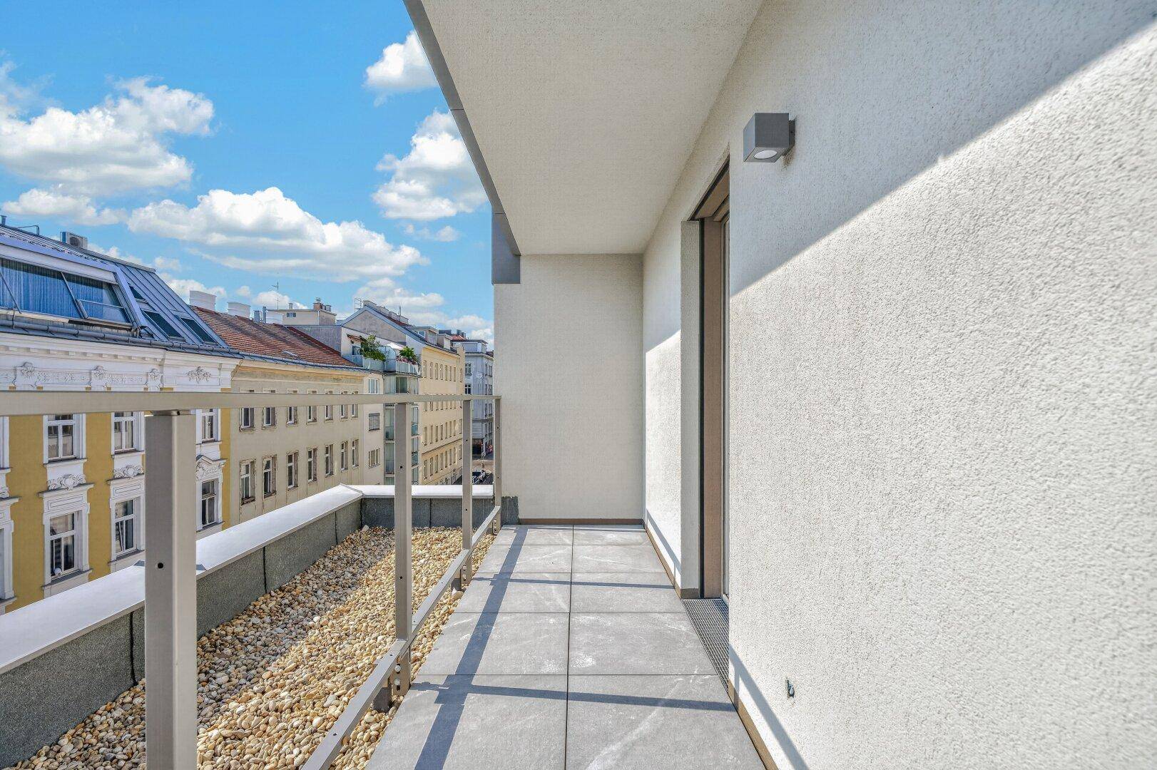 Heller Balkon mit schlichtem Design, Fliesenboden und Blick auf die umliegende Bebauung.