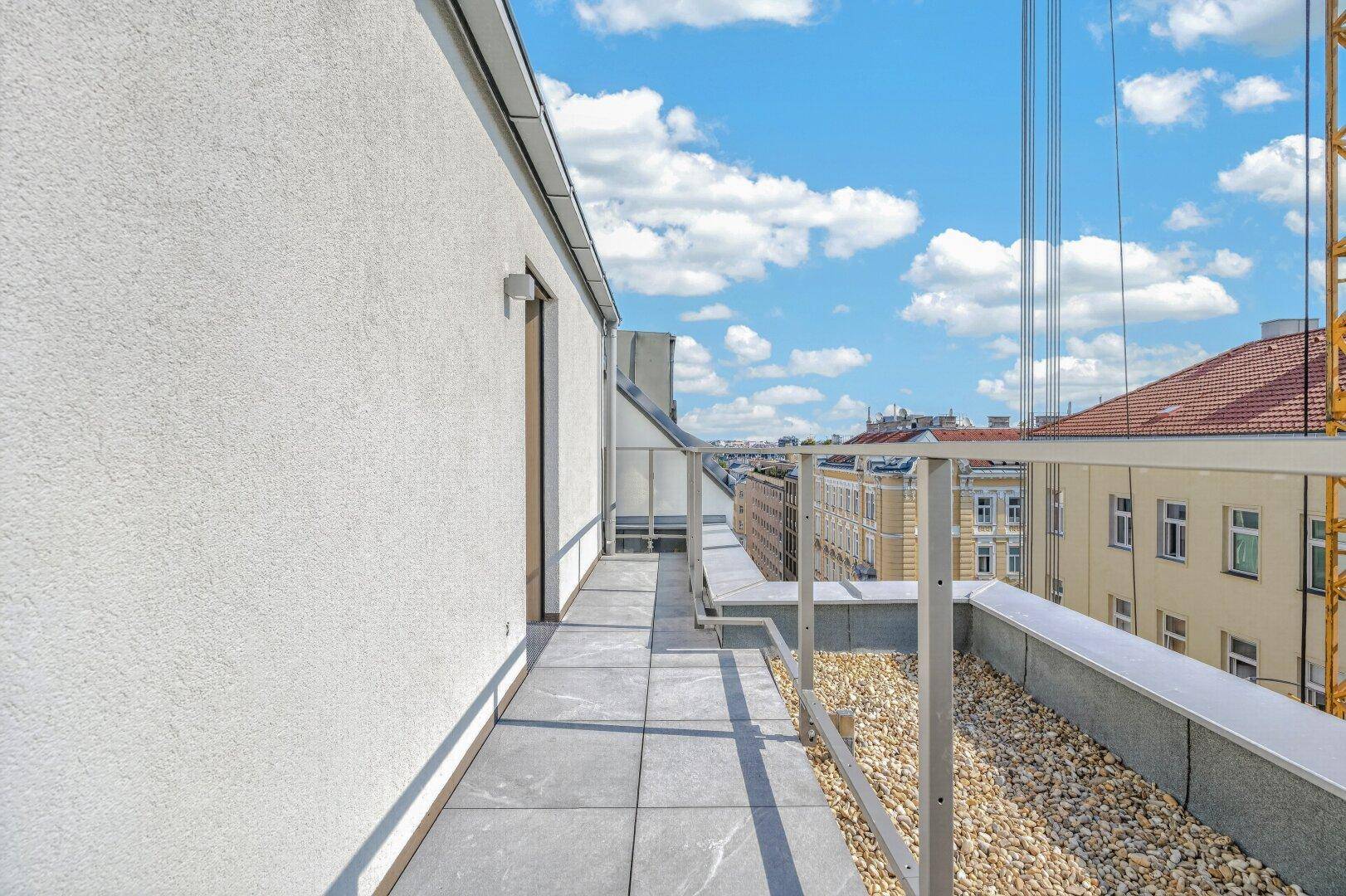 Moderner Balkon mit Fliesen und Kies, bietet einen weiten Blick über die Dächer der Stadt.