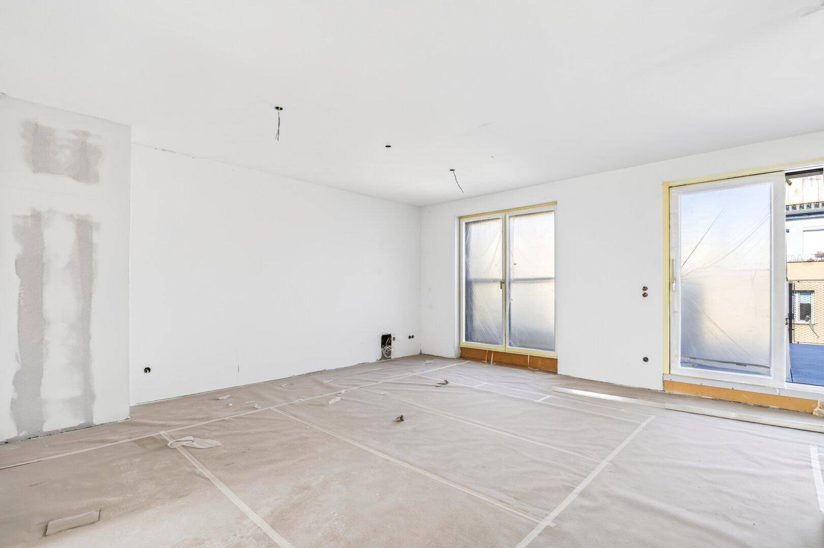 Großer Rohbau mit viel Tageslicht durch Fenster und Schiebetür zum Außenbereich.