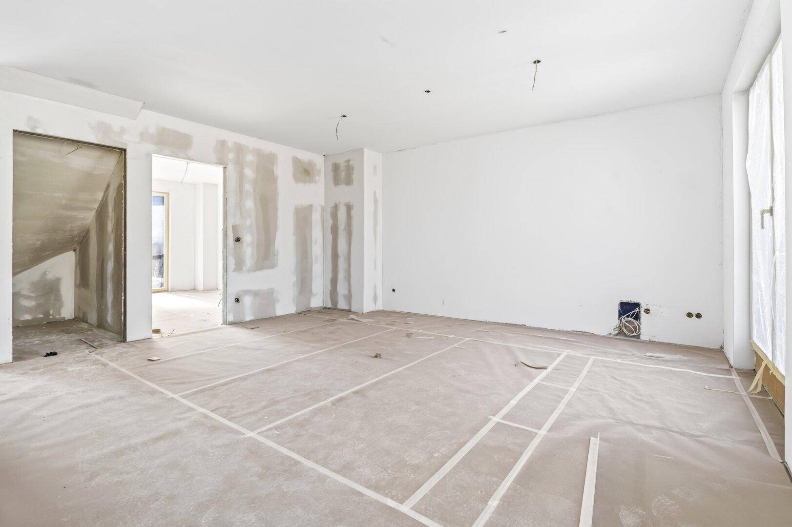 Rohbau eines hellen Raumes mit vorbereiteten Wänden und Decken, bereit für den Innenausbau.