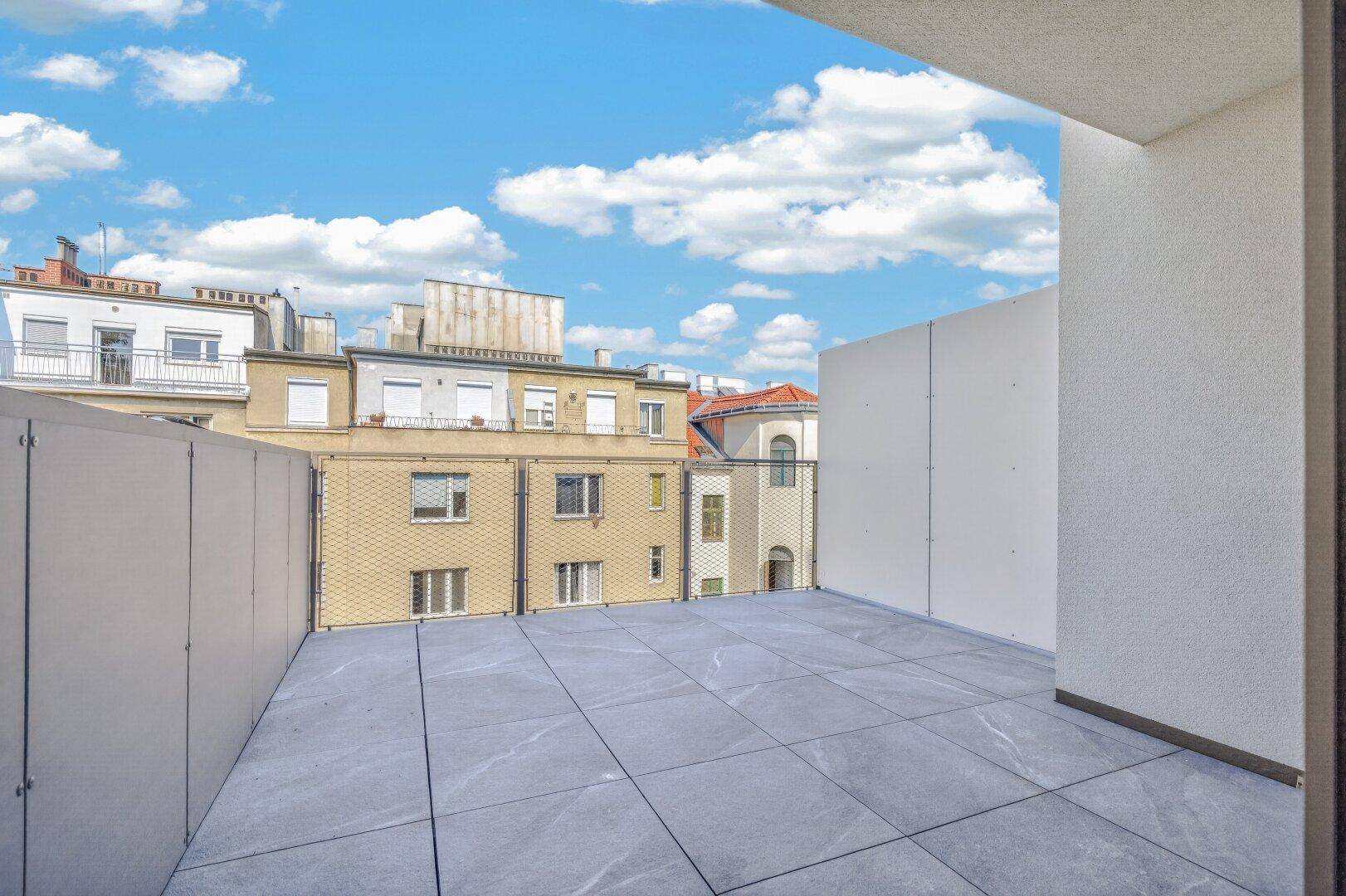 Helle Terrasse mit großformatigen Fliesen und weitem Blick über die umliegenden Stadtgebäude.
