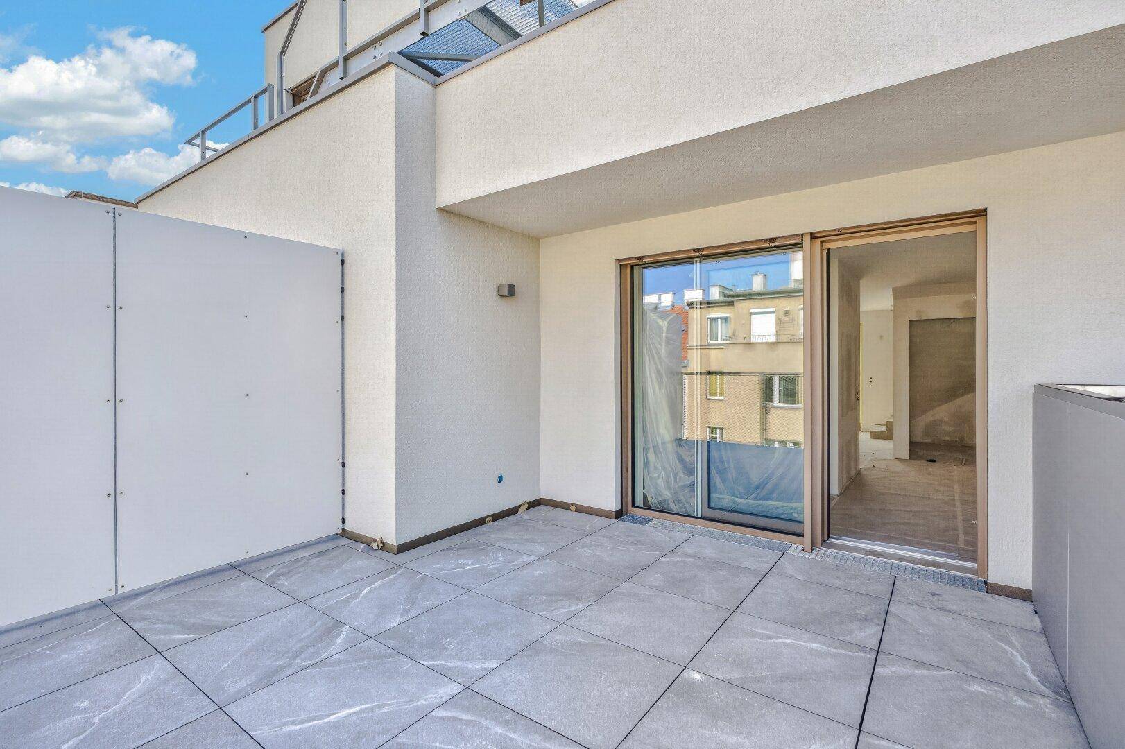 Moderne Terrasse mit grauen Fliesen und Schiebetür, die den Übergang zum Wohnraum ermöglicht.