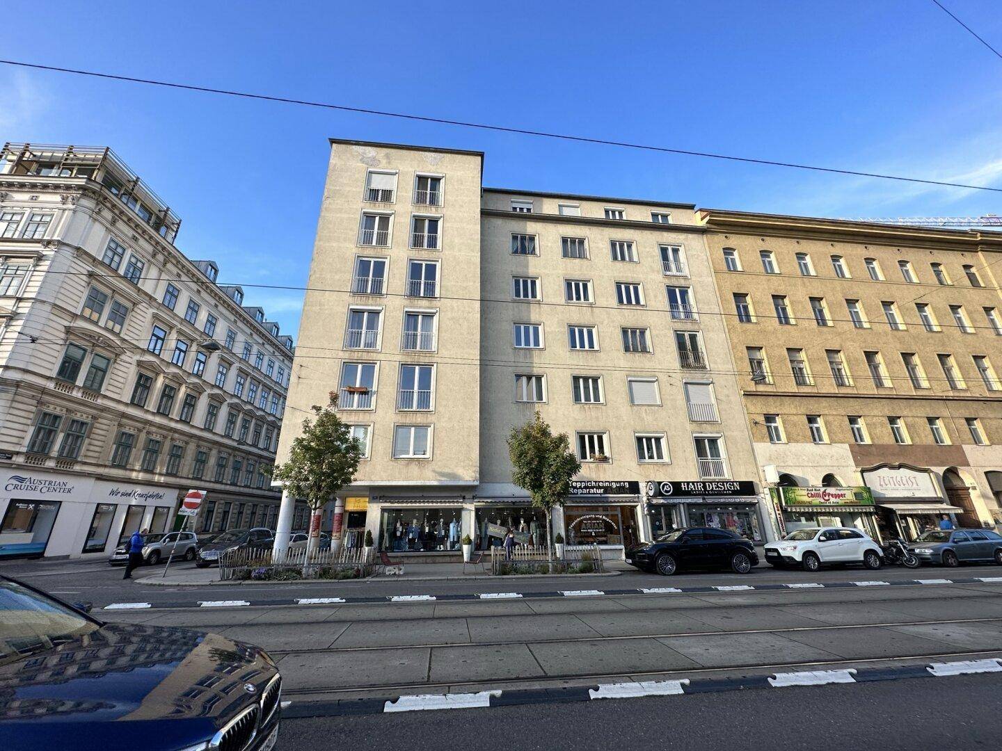 Mehrstöckiges Gebäude an einer belebten Stadtstraße mit Geschäften im Erdgeschoss.