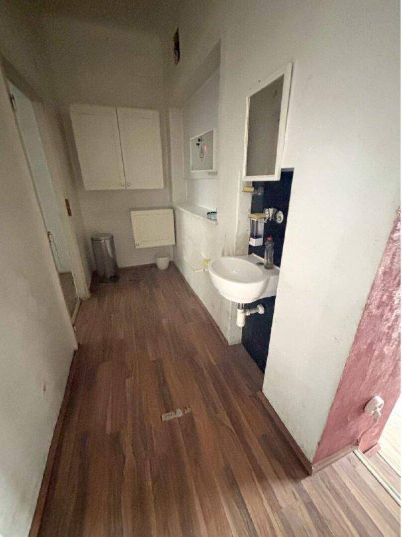 Kleiner Raum mit Waschbecken, Spiegelschrank und Laminatboden, möglicherweise ein Gäste-WC oder Abstellraum.