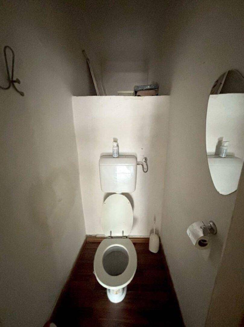 Enges Gäste-WC mit einfacher Toilette, kleinem Spiegel und Laminatboden.