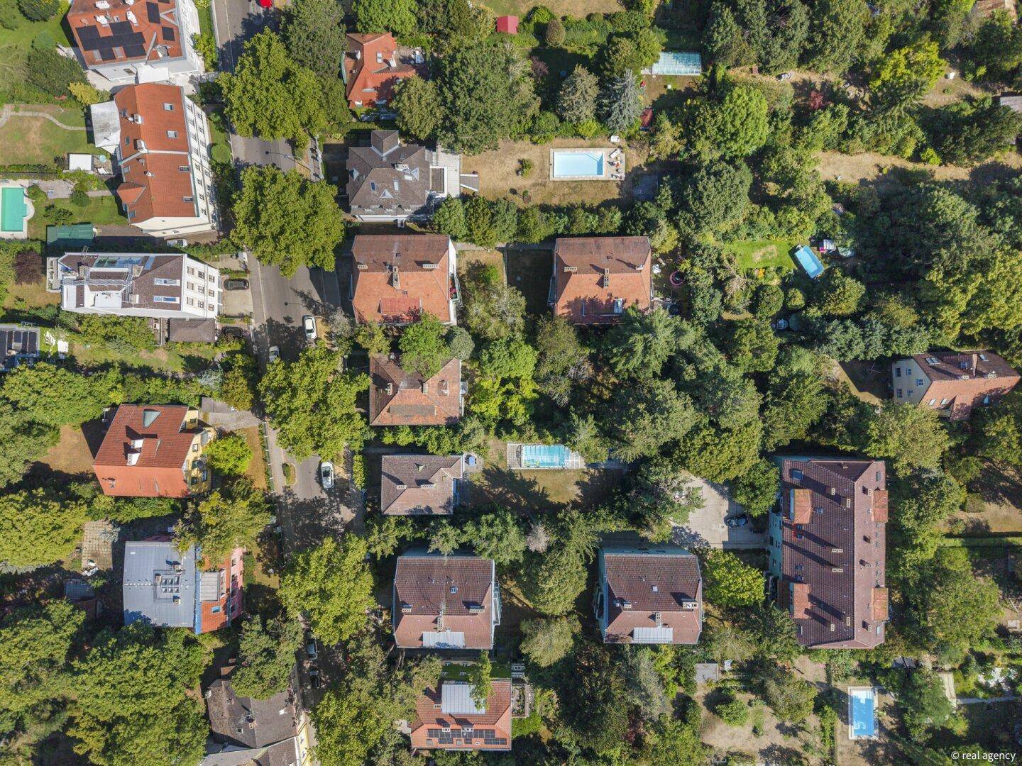 Weitläufige Luftaufnahme einer grünen Wohnsiedlung mit zahlreichen Häusern und Gärten.