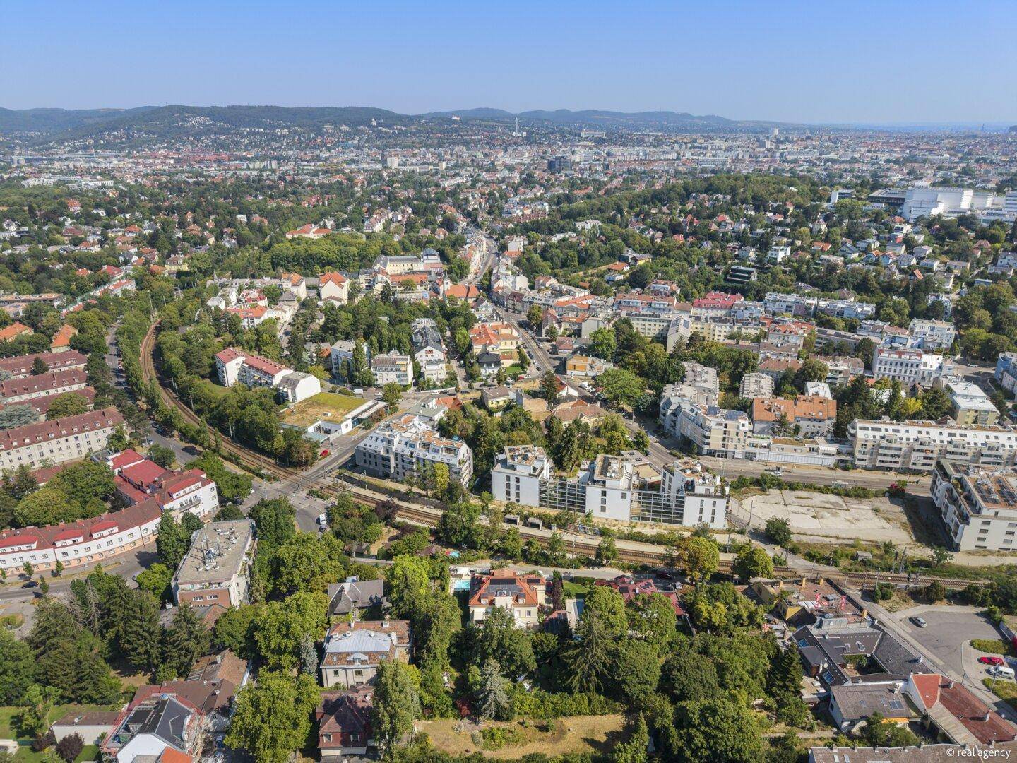 Panoramablick über eine weitläufige Stadtlandschaft mit grünen Hügeln im Hintergrund.