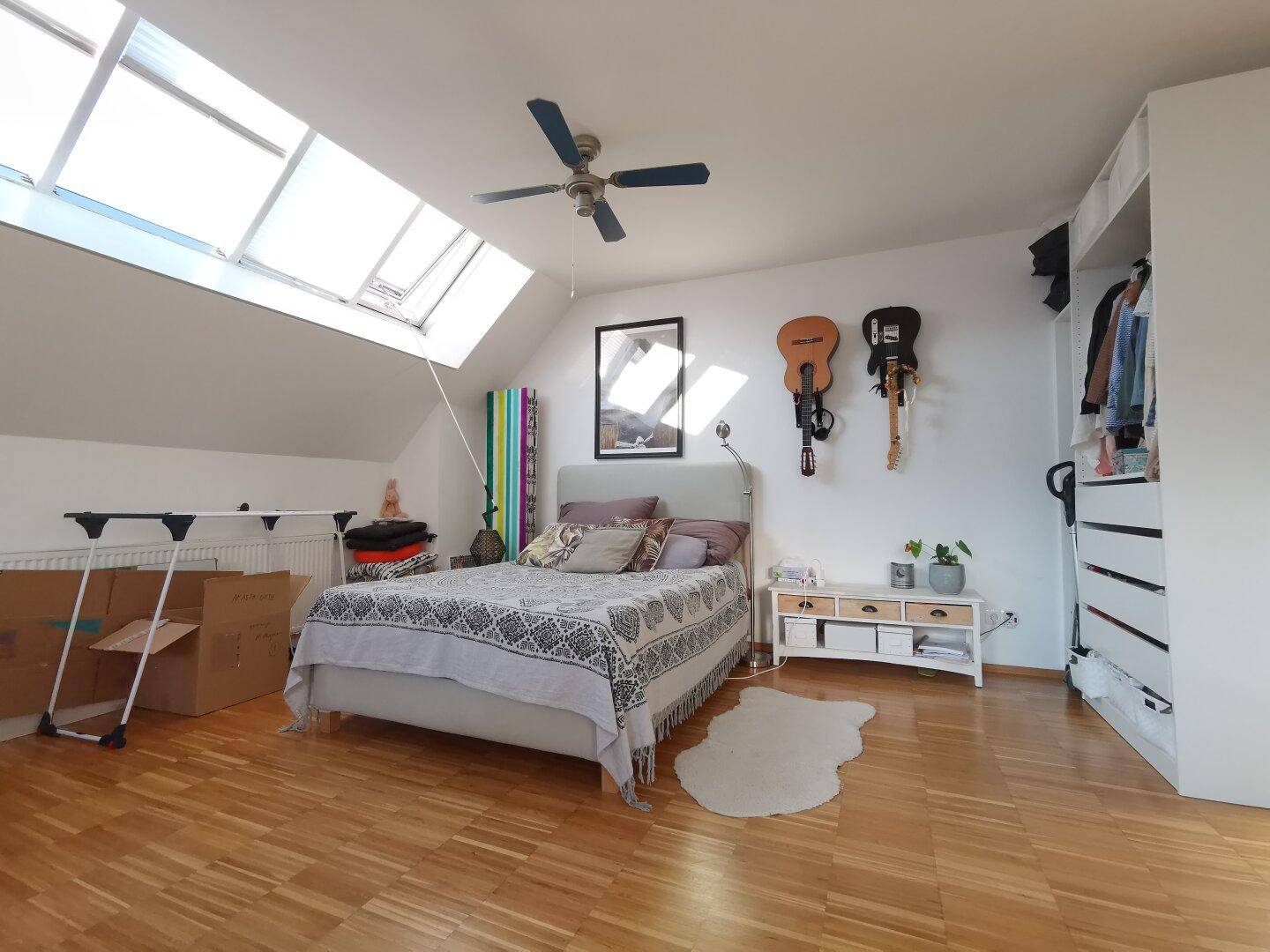 Schlafzimmer mit Holzboden, Dachfenstern, Deckenventilator und offenem Kleiderschrank.