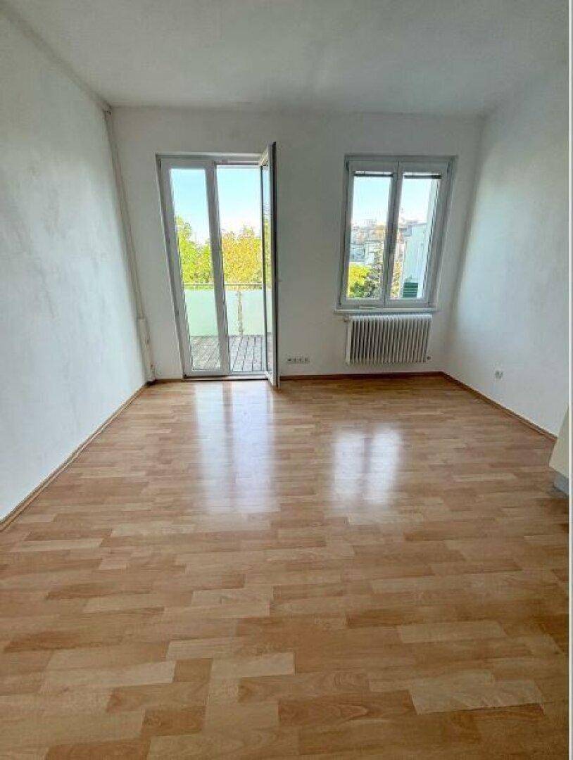 Heller Raum mit Laminatboden, weißen Wänden und einer Balkontür, die viel Licht spendet.