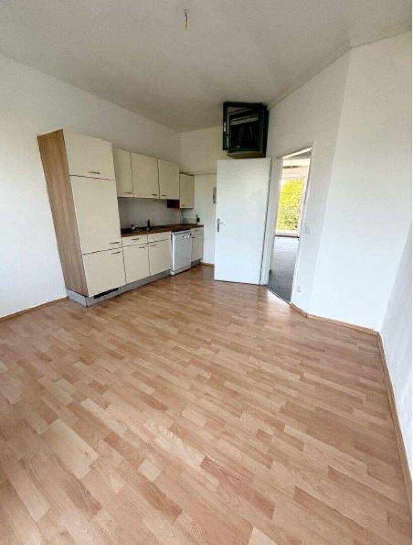 Raum mit kleiner Küchenzeile, Laminatboden und hellen Wänden, ideal für eine kompakte Wohnlösung.