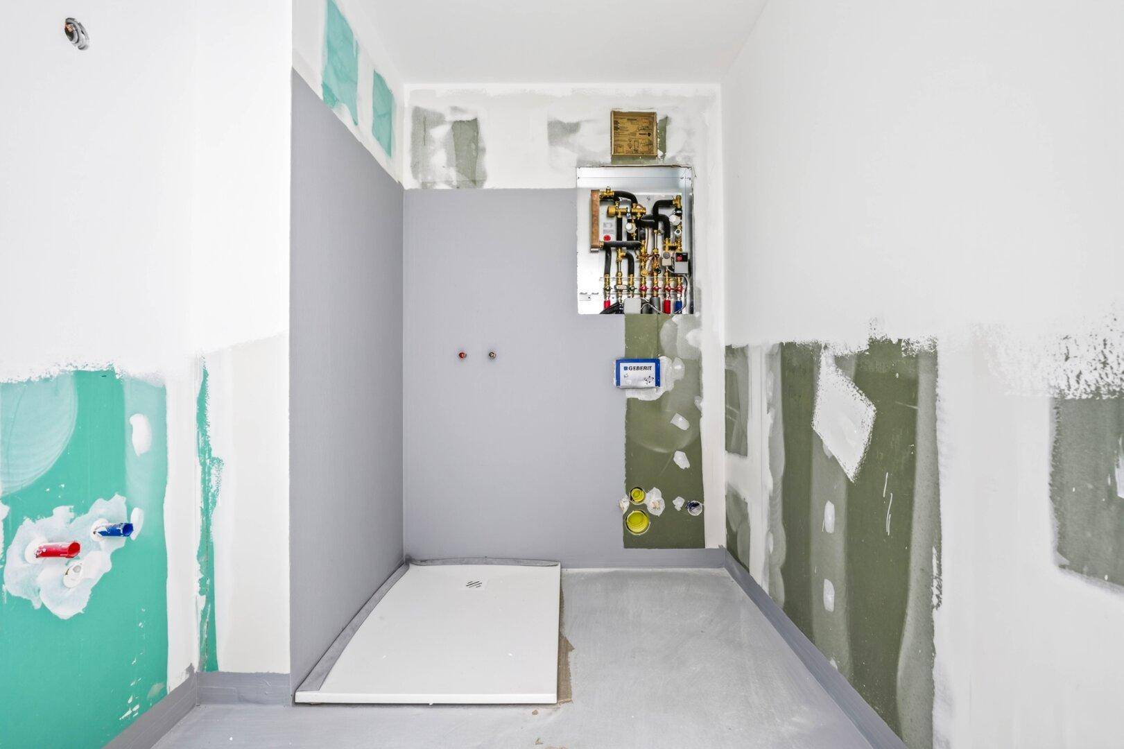 Unfertiges Badezimmer mit sichtbaren Installationen und vorbereiteter Duschwanne.