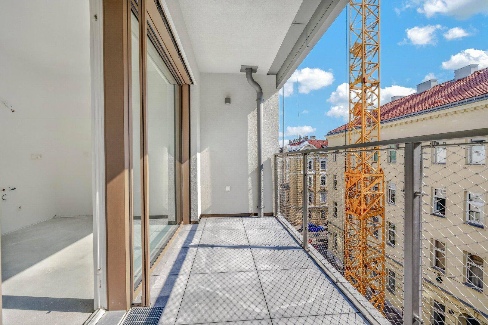 Heller Balkon mit Fliesenboden und Blick auf die Stadt und einen Baukran.