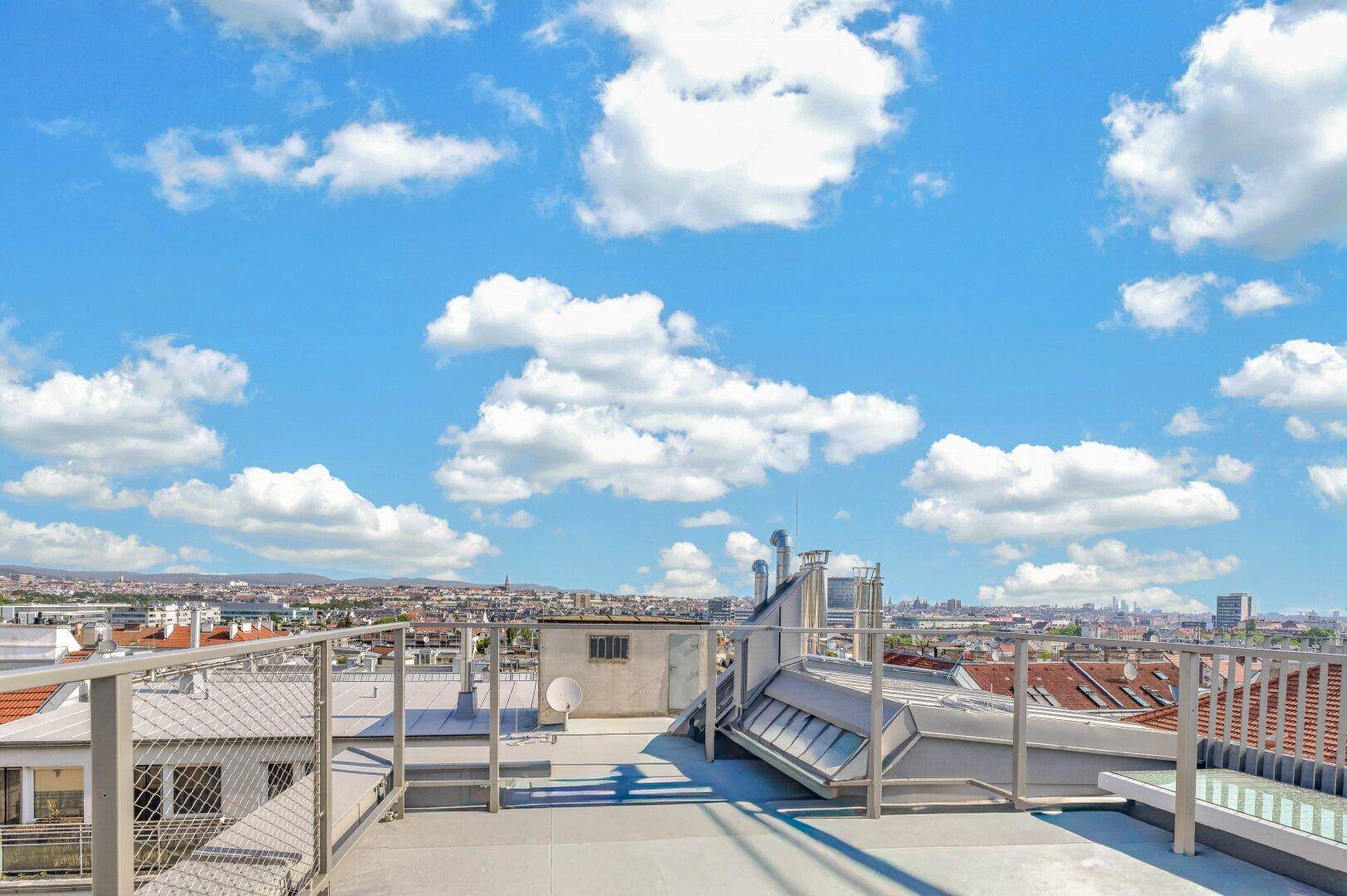 Helle Dachterrasse mit Fliesenboden und weitem Blick über die städtische Umgebung.