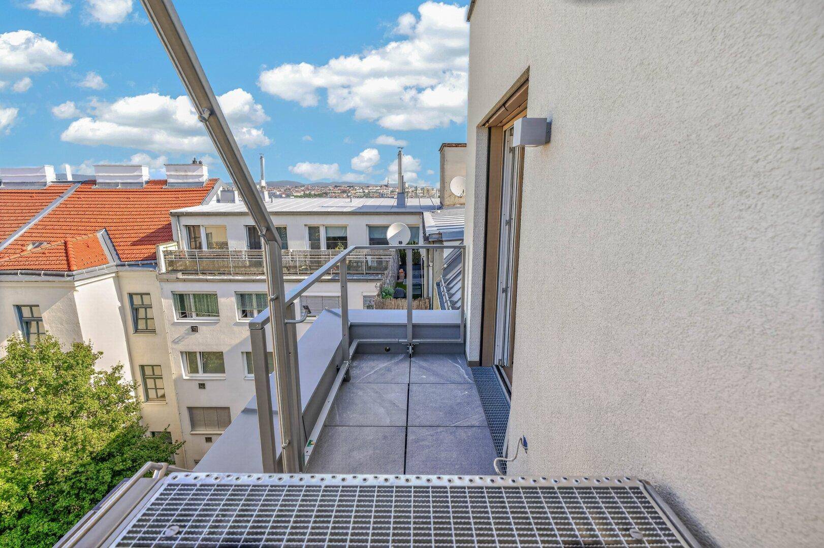 Kleiner Balkon mit Metallgitterboden und Zugang zu einem Innenraum mit Stadtblick.