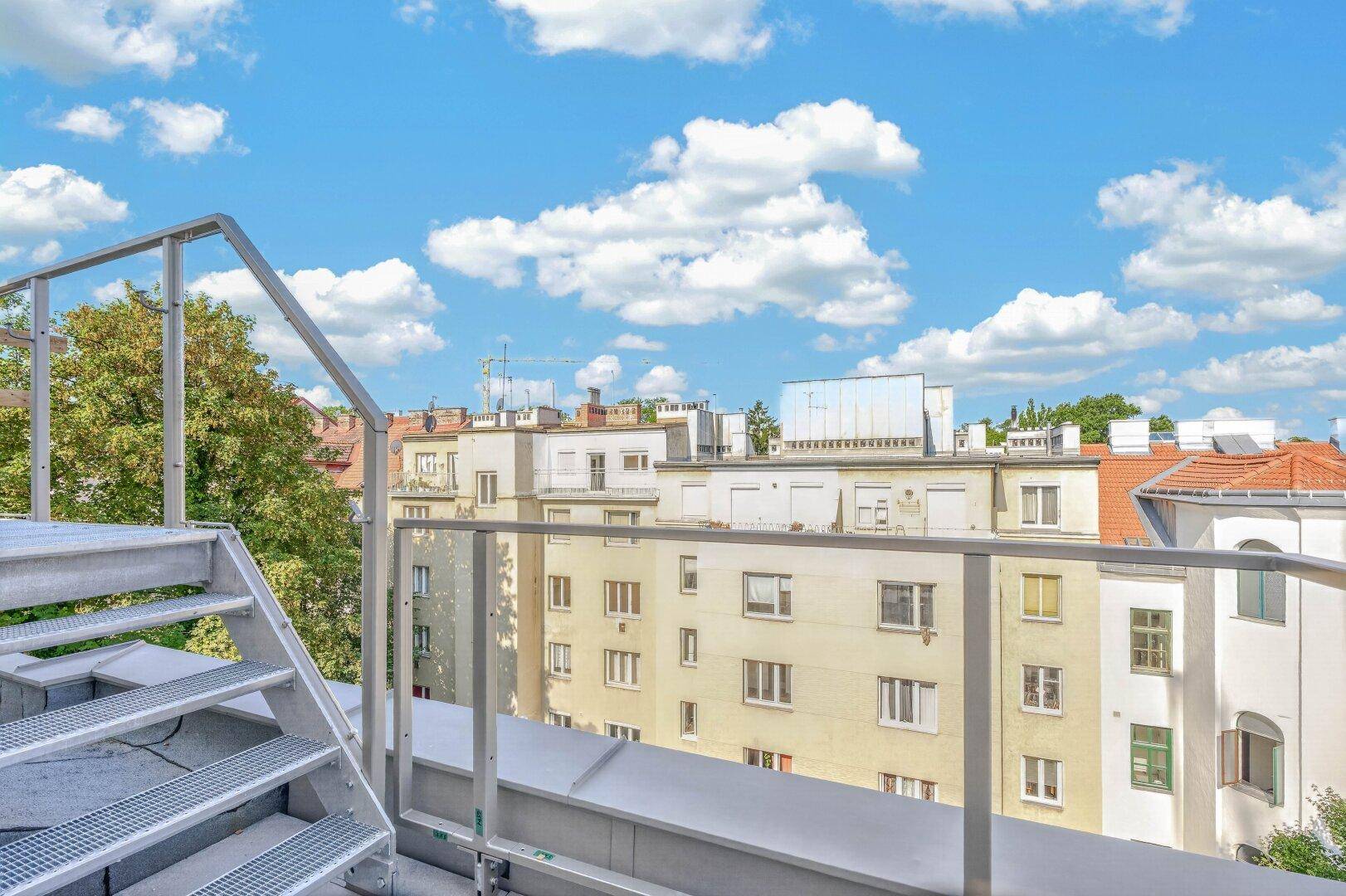 Metalltreppe führt zu einer oberen Ebene mit Glasgeländer und Blick auf die Stadt.