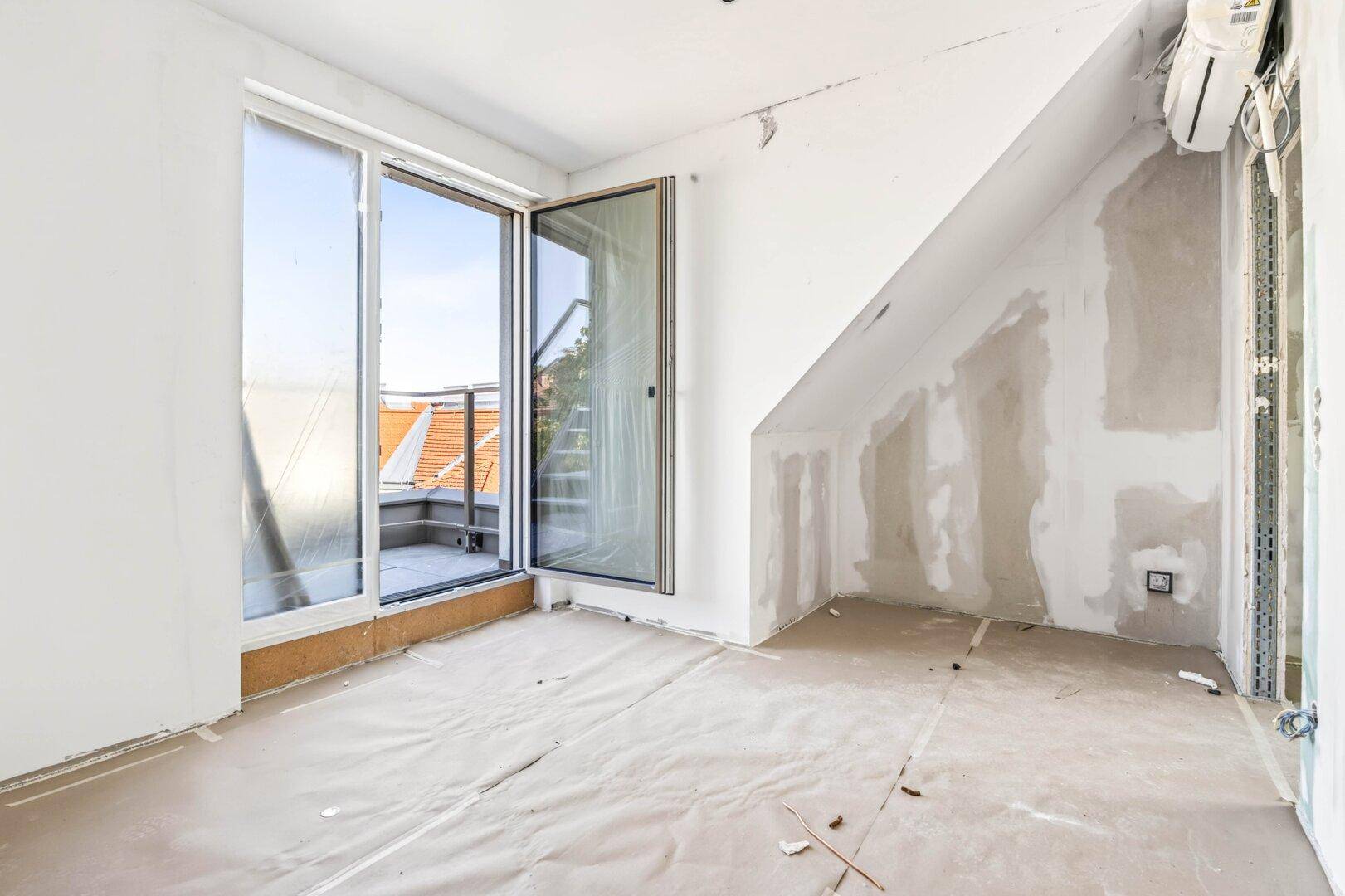 Helles Zimmer im Rohbau mit großer Schiebetür und Dachschräge, ideal für zukünftige Gestaltung.