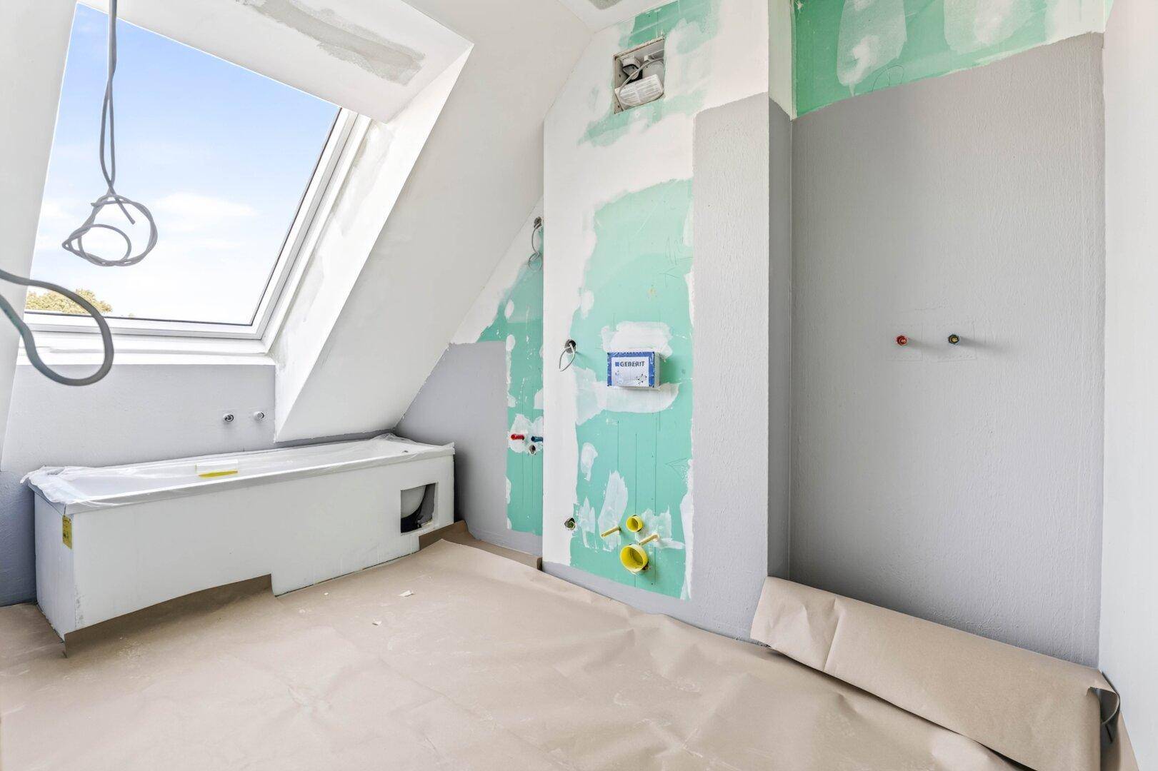 Badezimmer im Rohbau mit sichtbaren Installationen, Badewannenrahmen und Dachfenster.