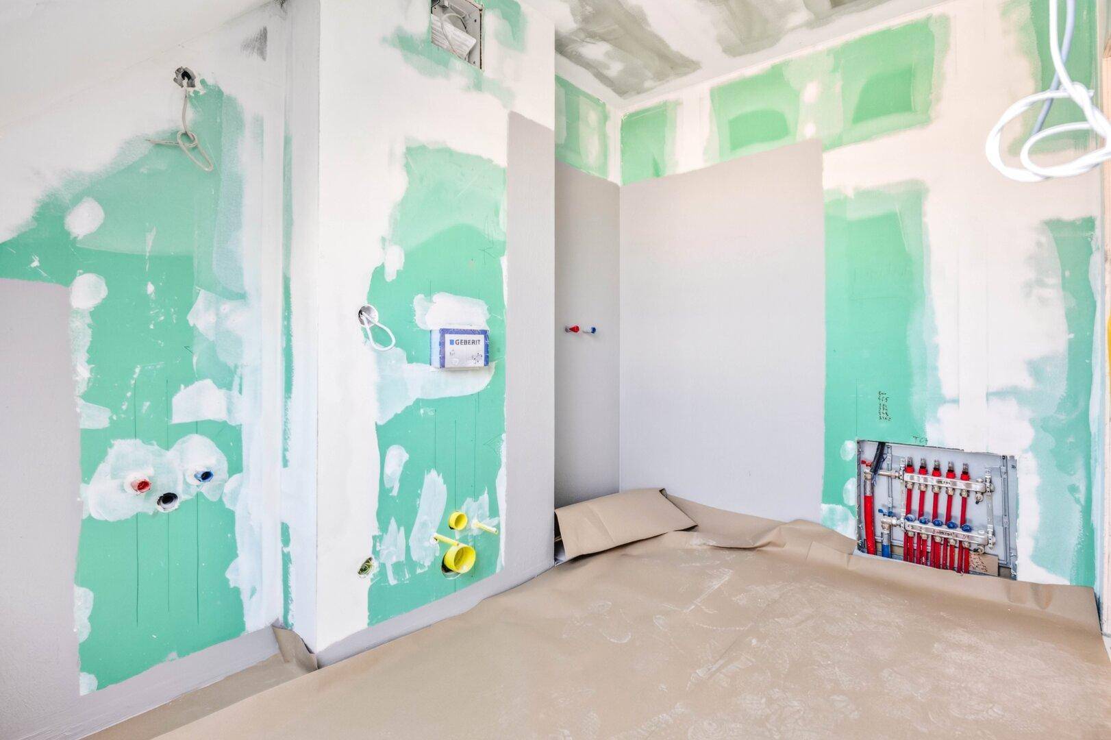 Badezimmer im Rohbau mit sichtbaren Wasserleitungen und vorbereiteten Wänden für den Ausbau.