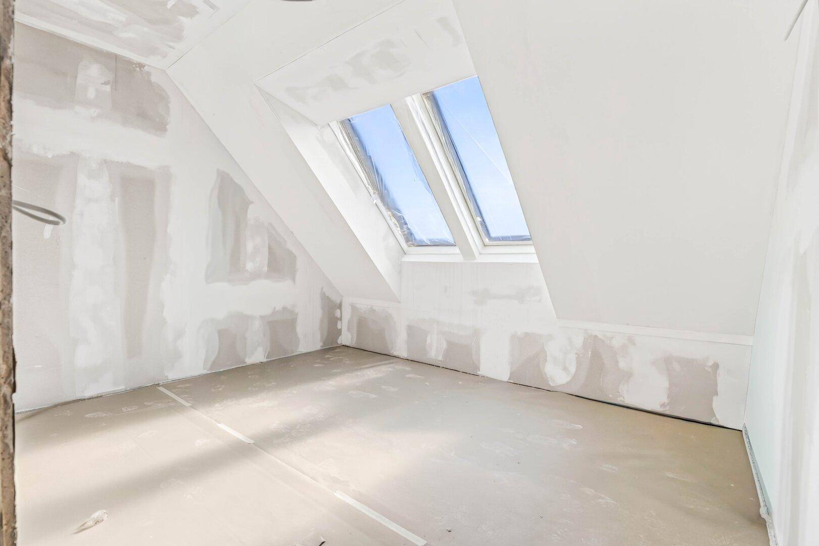 Helles Rohbauzimmer mit mehreren Dachfenstern und schräger Decke, viel natürliches Licht.