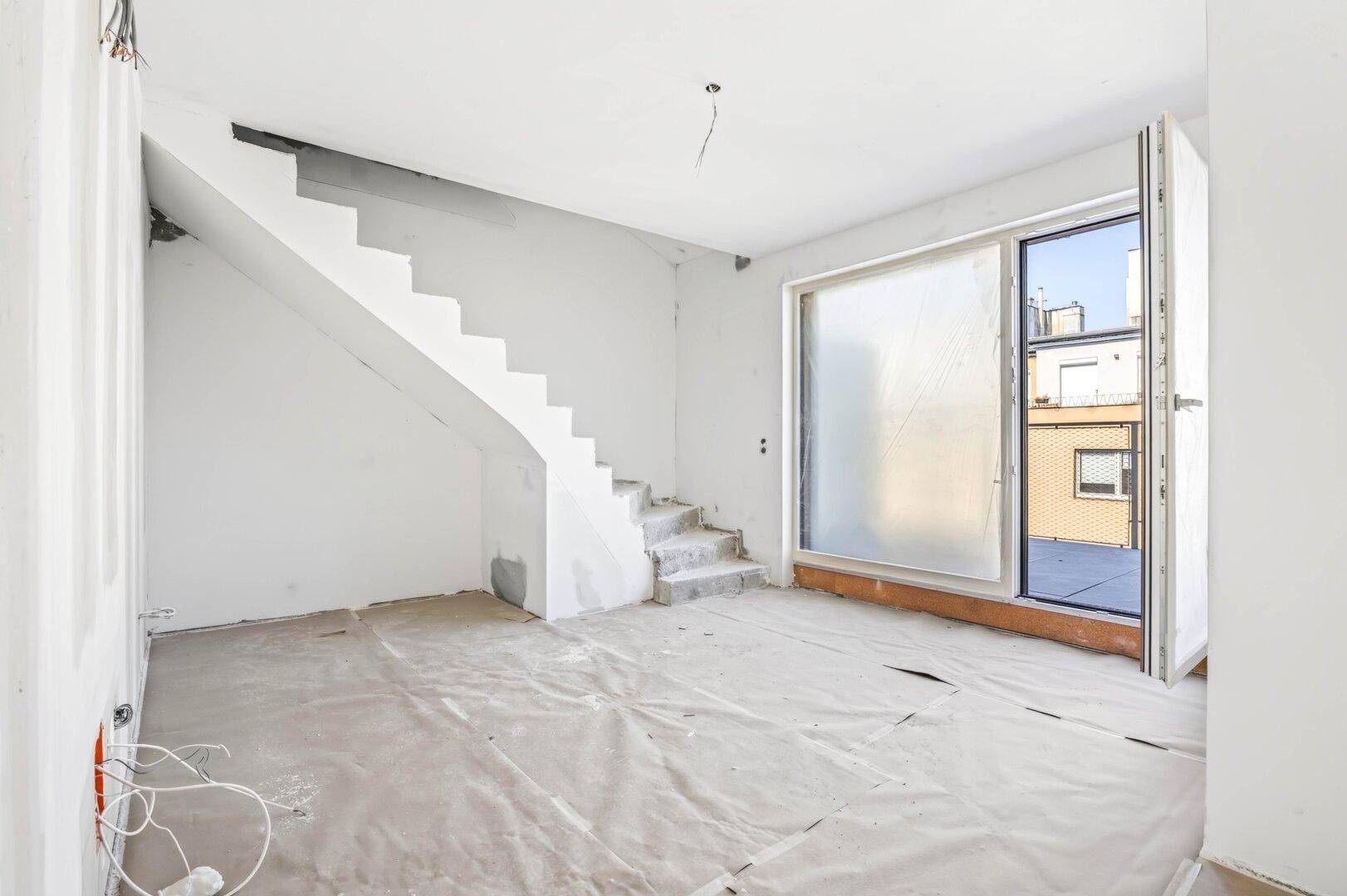 Rohbauzimmer mit Betontreppe und großer Schiebetür, viel Tageslicht und offenes Raumgefühl.