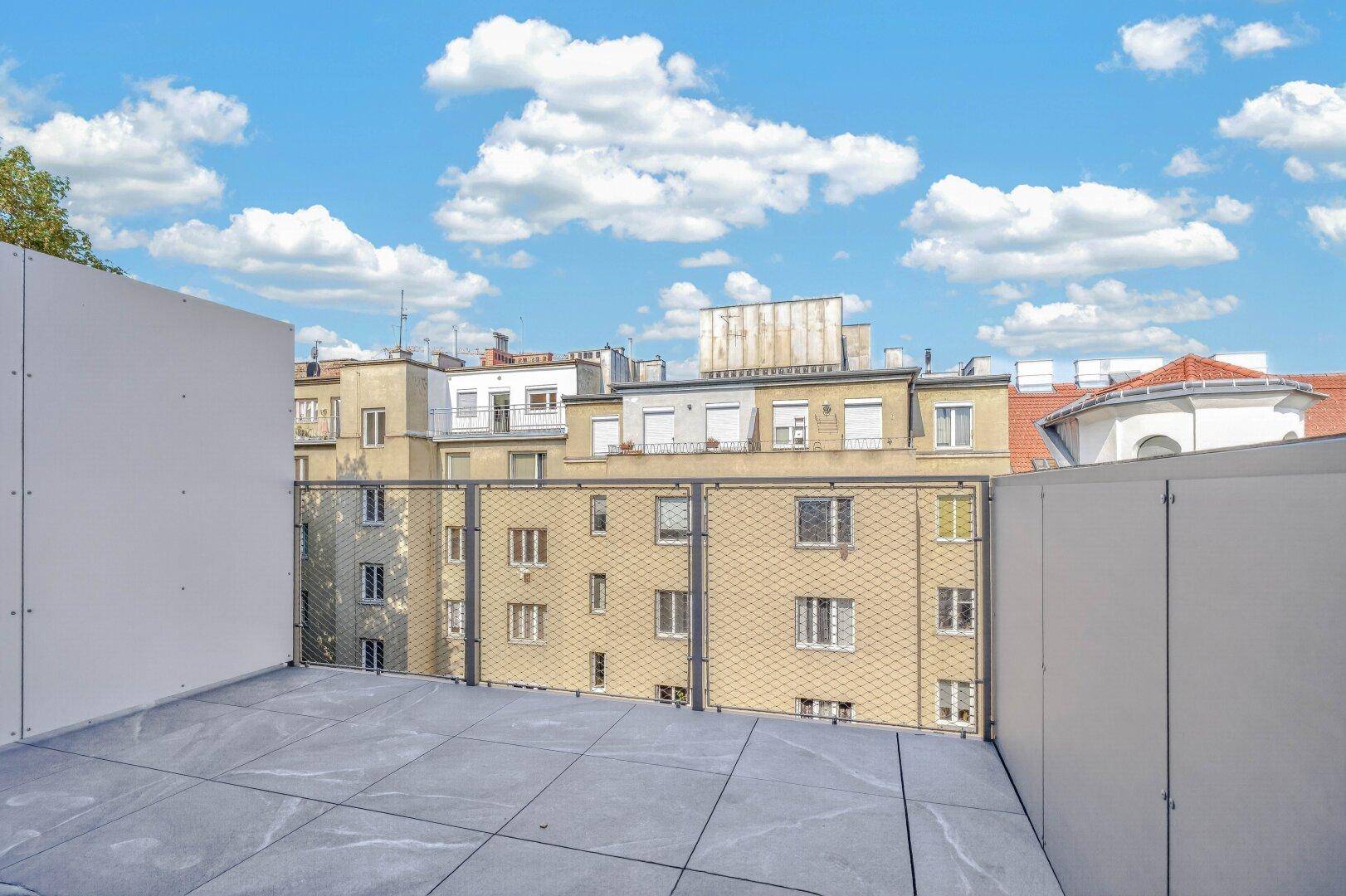 Moderne Dachterrasse mit Fliesenboden und Blick auf die umliegenden Gebäude der Stadt.