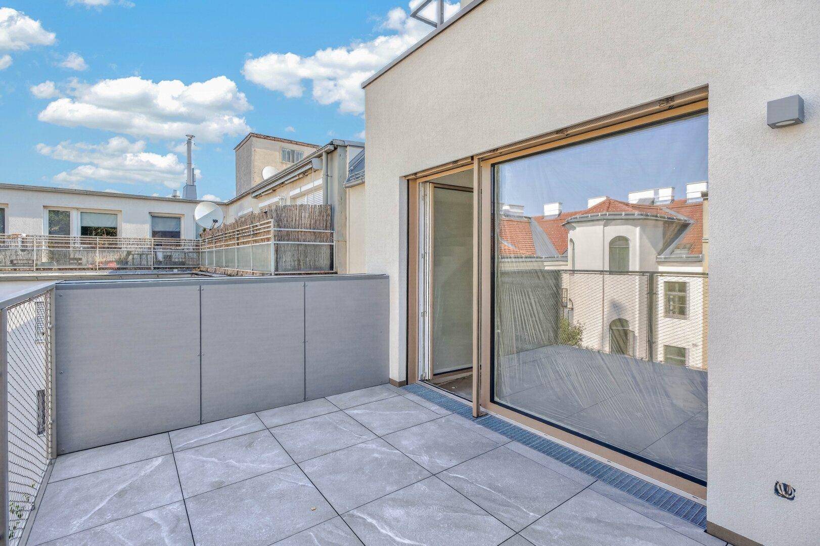 Heller Balkon mit Fliesenboden und großer Schiebetür, bietet Zugang zum Innenbereich.