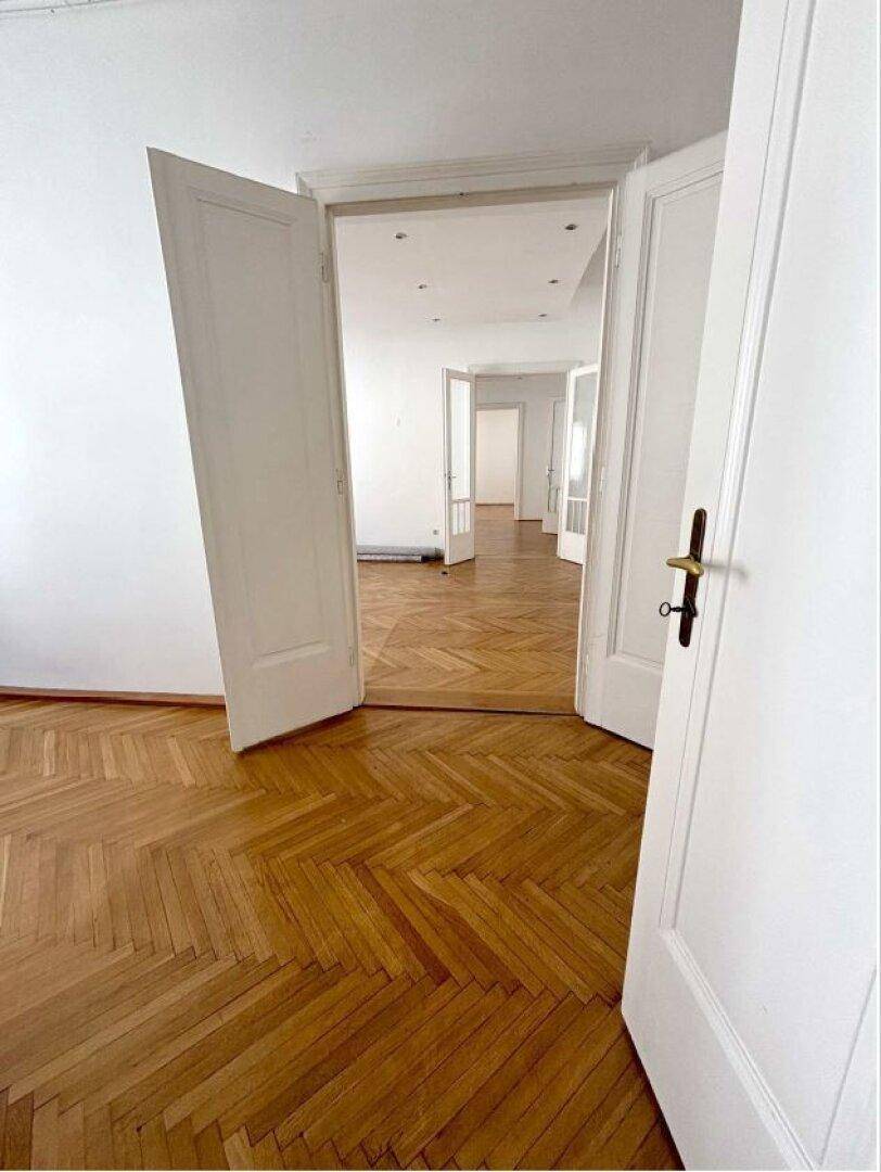 Blick durch mehrere offene Türen, die eine Reihe von Räumen mit Fischgrätparkett und hohen Decken verbinden.