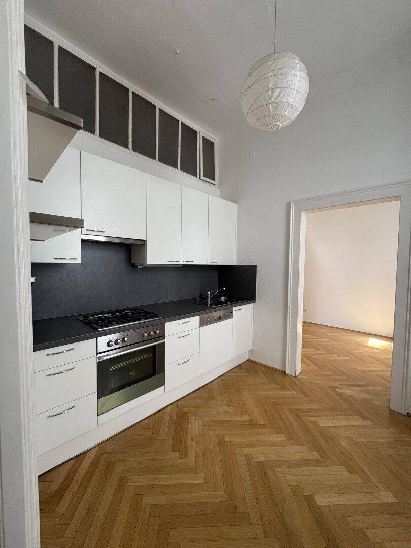 Moderne Einbauküche mit weißen Schränken, dunkler Arbeitsplatte und Fischgrätparkettboden.