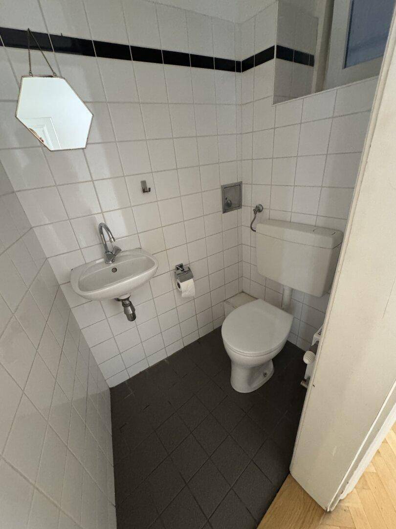 Kleines Gäste-WC mit weißen Fliesenwänden, dunklem Fliesenboden, Toilette und Waschbecken.