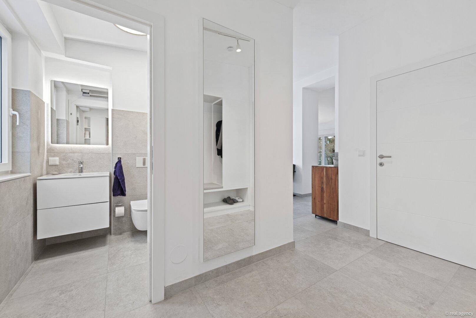 Heller Flur mit modernen Fliesen, großem Spiegel und Zugang zum Badezimmer.