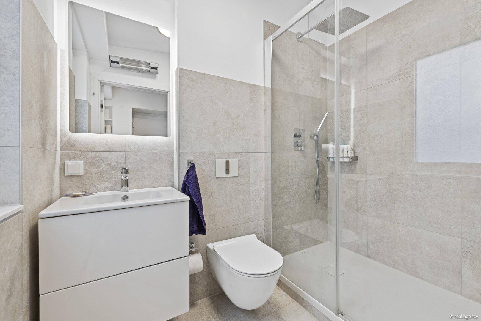 Modernes Badezimmer mit Dusche, wandhängendem WC und eleganten grauen Fliesen.